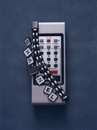 Chanel letter charm watch draped across a vintage grey remote control against a dark blue background.