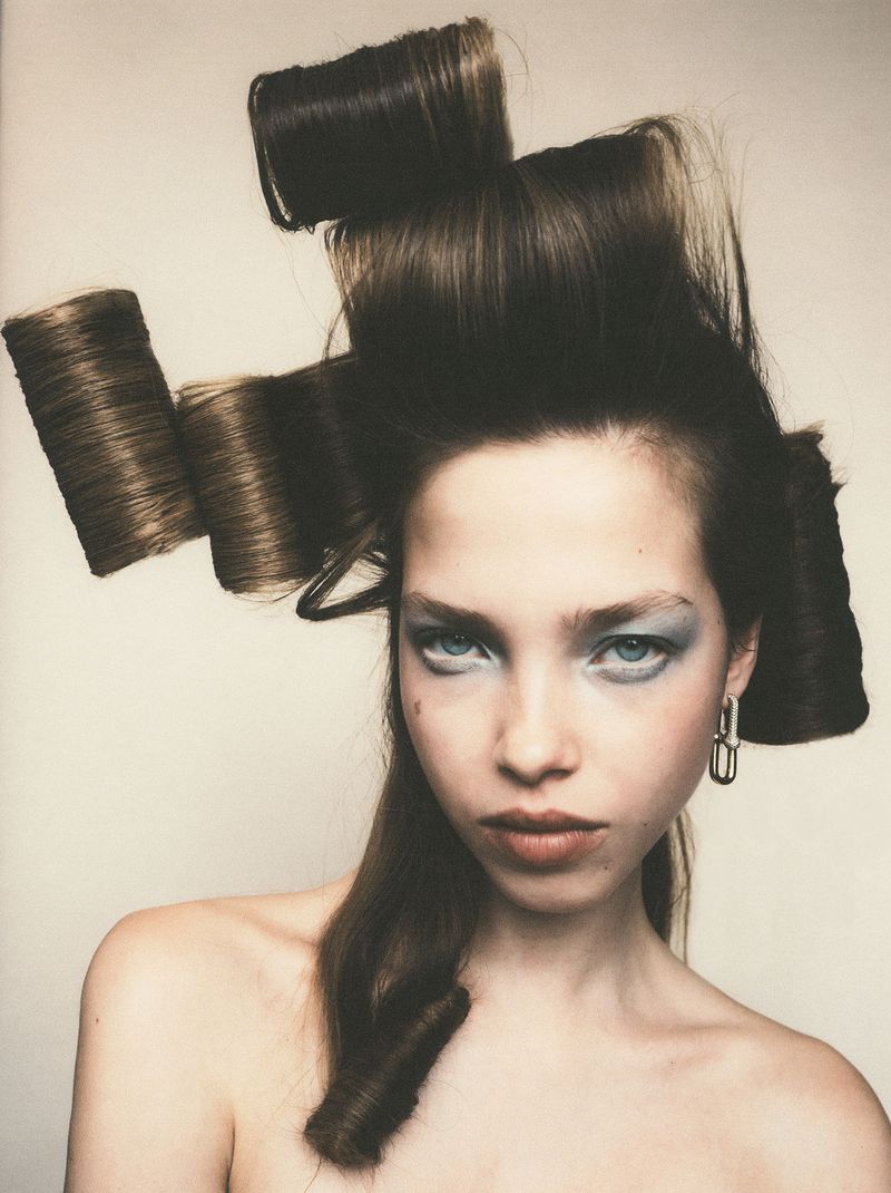 Model Mirte Rooze with sculptural cylindrical hair rolls and pale blue eyeshadow against an off-white background.