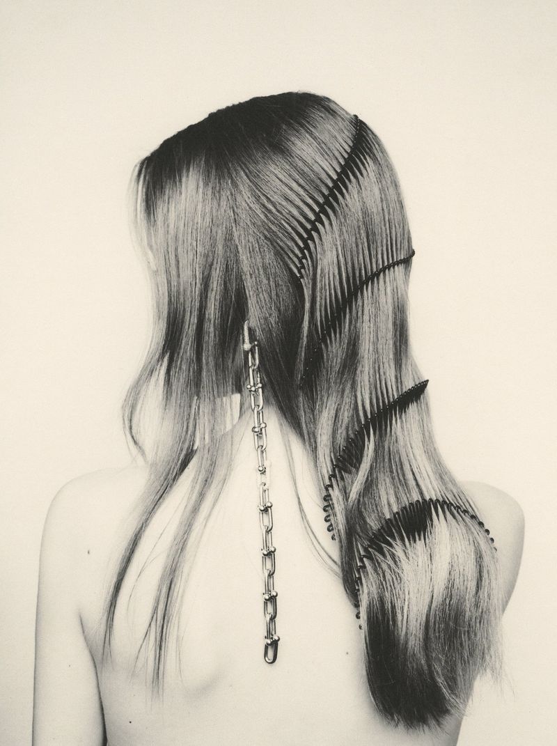 Back view of a model with long hair styled with interwoven black combs and a silver chain earring against a light backdrop.