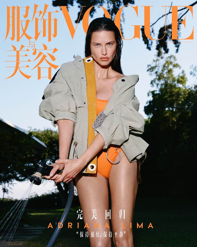Vogue cover featuring Adriana Lima in an orange swimsuit and jacket, holding a garden hose with greenery and blue sky in background.