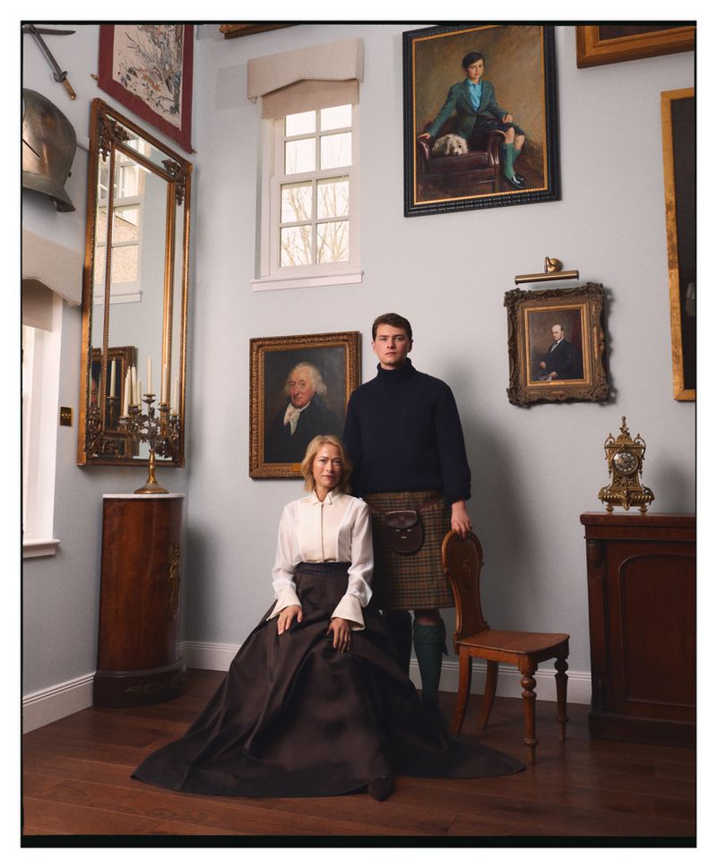 Woman in a white blouse and dark ball skirt seated beside a man in a black turtleneck and tartan kilt in an art-filled room.