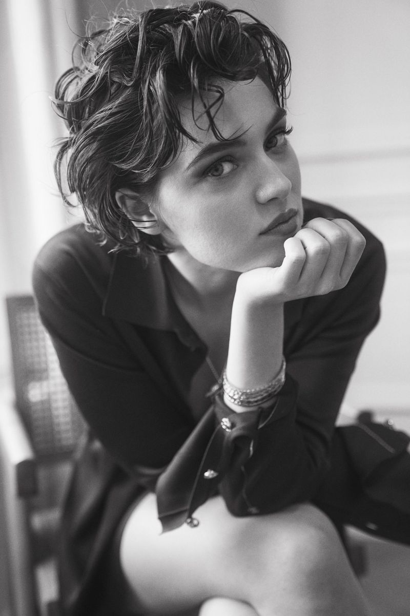 Black and white portrait of a woman with short wavy hair resting her chin on her hand in a dark shirt.