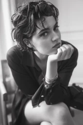 Black and white portrait of a woman with short wavy hair resting her chin on her hand in a dark shirt.
