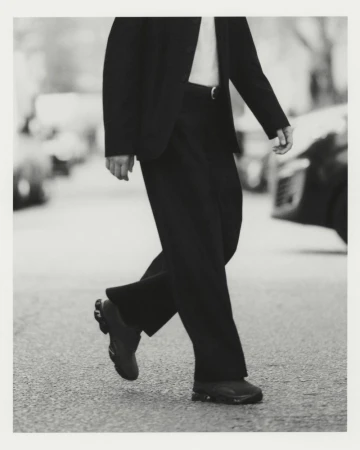 Cropped view of a model walking on a city street wearing wide-leg trousers, a tailored dark jacket, and sneakers.