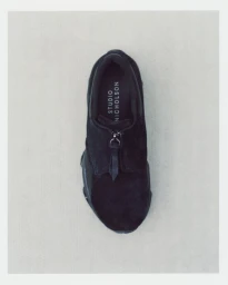 Top-down view of a black Studio Nicholson sneaker with a front zipper closure against a light neutral background.