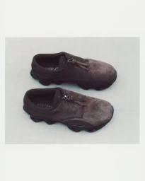 Pair of brown suede zip-up sneakers with sculpted dark outsoles resting on a neutral light surface.