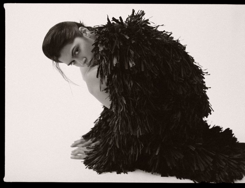 Model in a dark fringed coat posing against a plain background for M Revista de Milenio siluetas en tension editorial