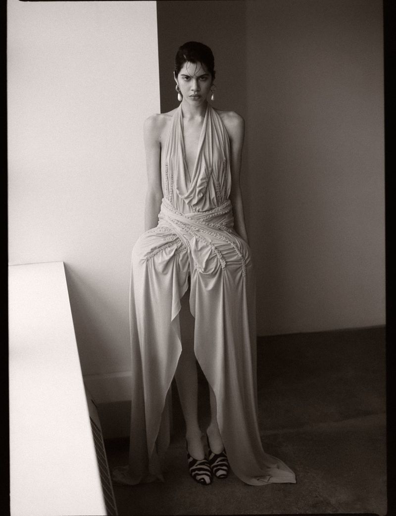 Valeria Gomez wearing a draped sculptural halter gown and striped heels in a monochrome editorial portrait.