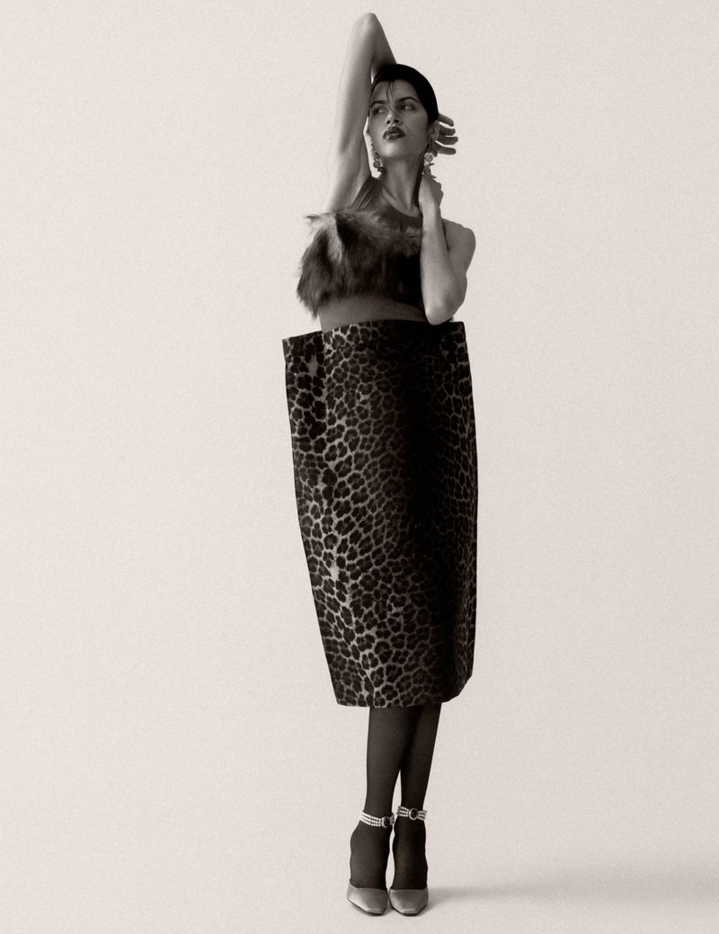 Model posing in a structured leopard print dress with a raised arm against a seamless studio background in black and white.