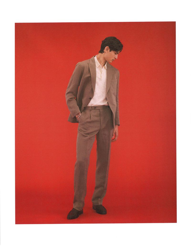 Model Ellis Mueller standing in a taupe tailored suit and white polo shirt against a vibrant red backdrop.