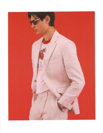 Model Ellis Mueller wearing a light pink linen suit and dark sunglasses against a bold red studio background.