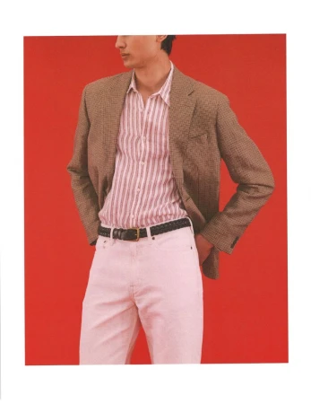 Model Ellis Mueller wearing a brown checked blazer, striped button-up shirt, and white pants against a bold red studio background.