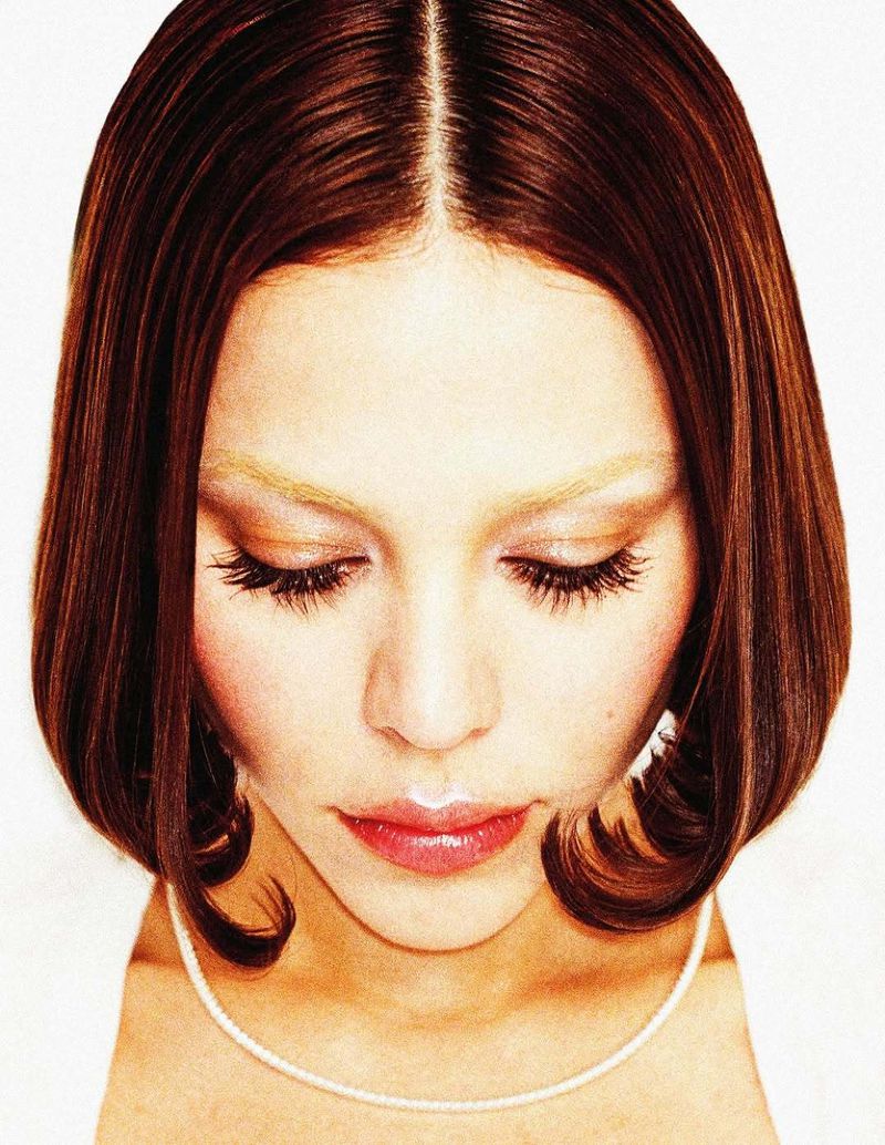 Close-up beauty portrait of a woman looking down, featuring a sleek auburn bob with flipped ends against a white background.