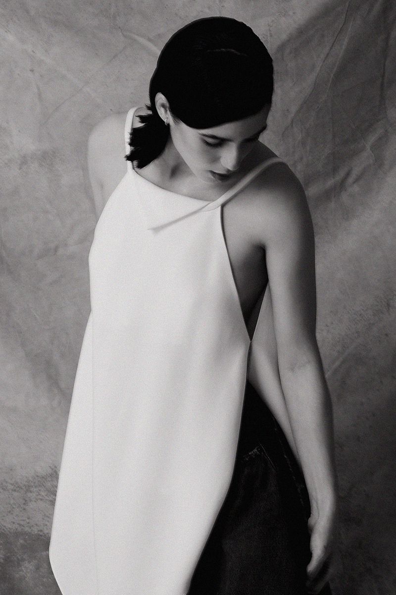 Woman in a white top wearing dark clothing against a textured backdrop