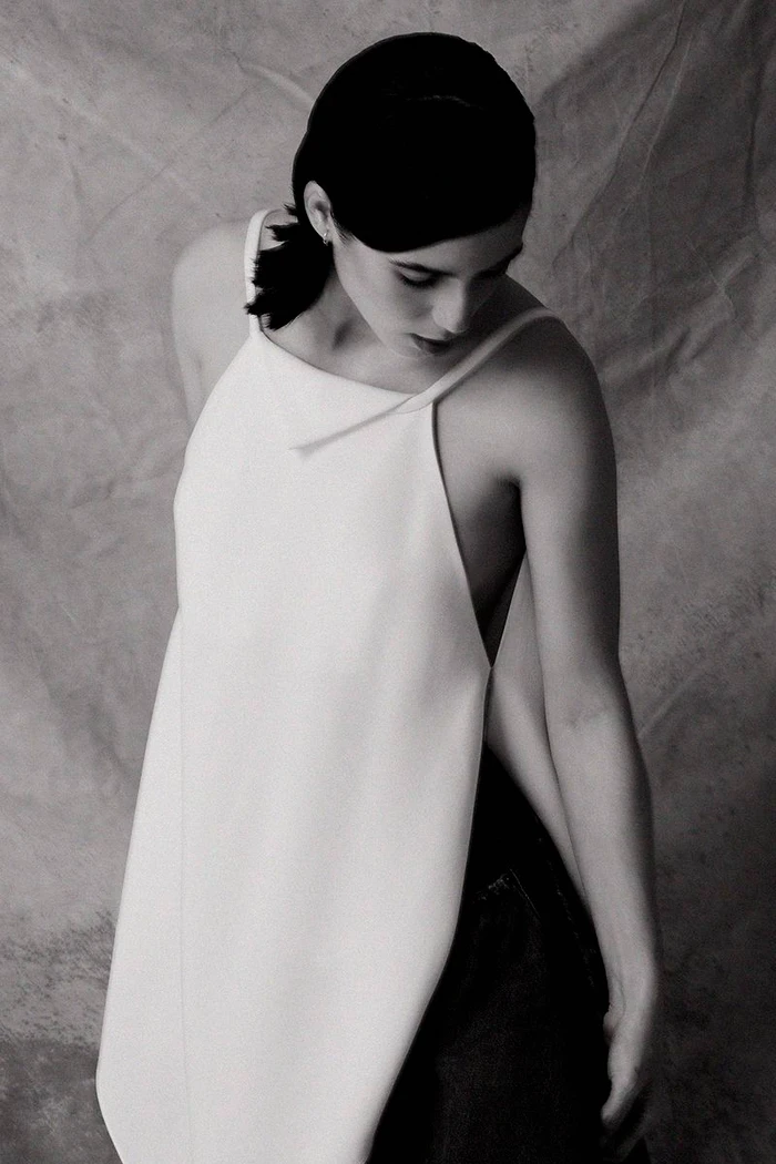 Woman in a white top wearing dark clothing against a textured backdrop
