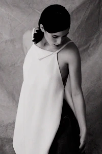 Woman in a white top wearing dark clothing against a textured backdrop