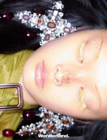 Close-up beauty editorial portrait of an East Asian model with closed eyes, yellow eyelashes, and ornate crystal drop earrings.