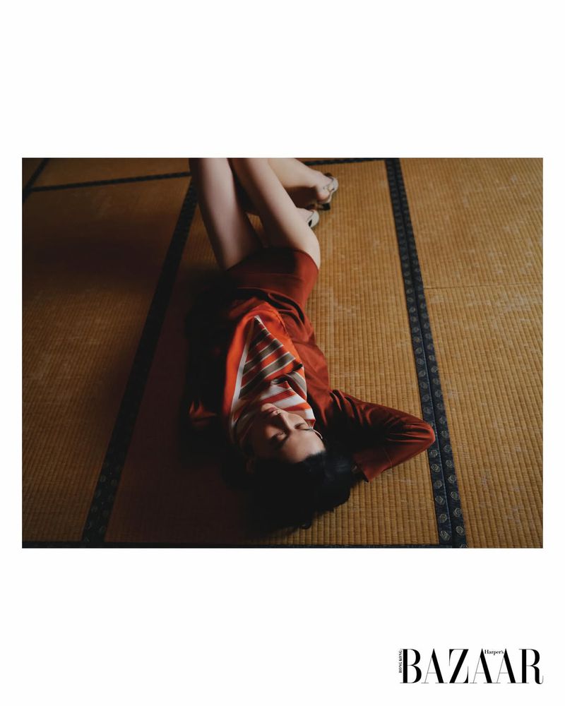 A woman lying on a traditional tatami floor wearing a rust-colored dress and striped neck scarf for a fashion magazine editorial.