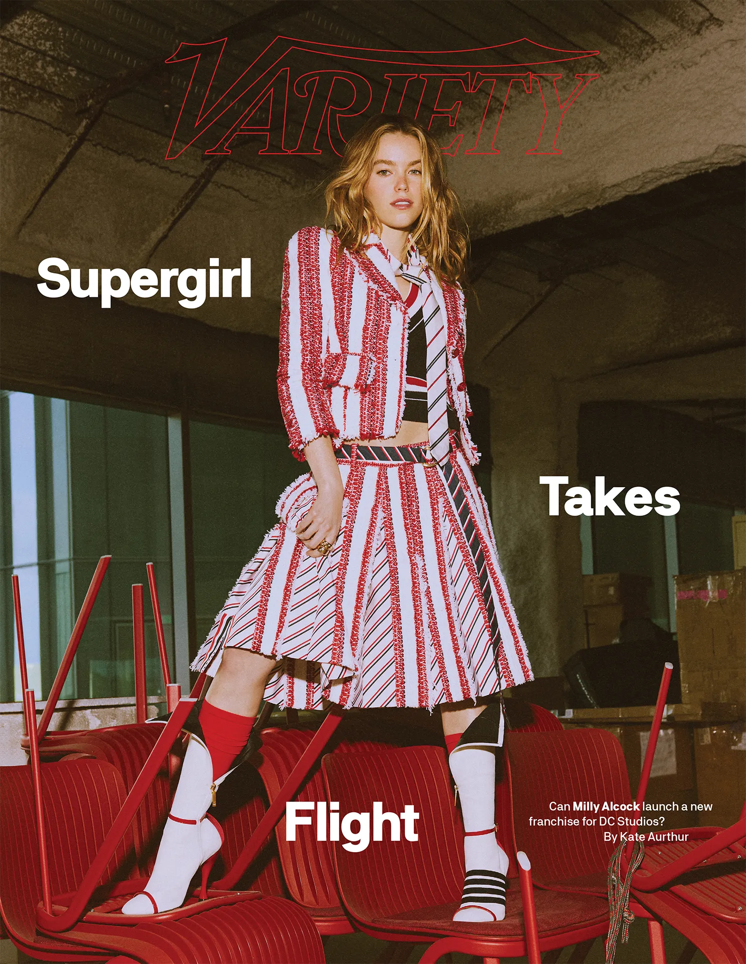 Actor Milly Alcock in a red and white striped tweed suit standing on stacked red chairs for Variety Magazine.