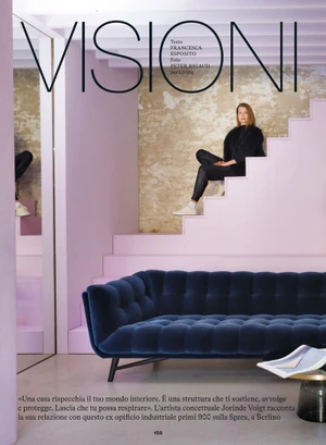 Artist Jorinde Voigt sitting on pastel pink steps above a dark blue tufted sofa in a modern interior magazine editorial.