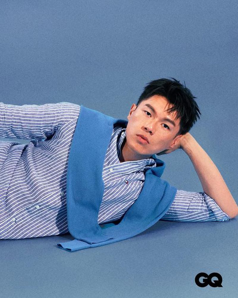 Actor Will Or reclining on a blue backdrop wearing a blue and white striped shirt with a blue sweater over his shoulders for GQ Hong Kong.