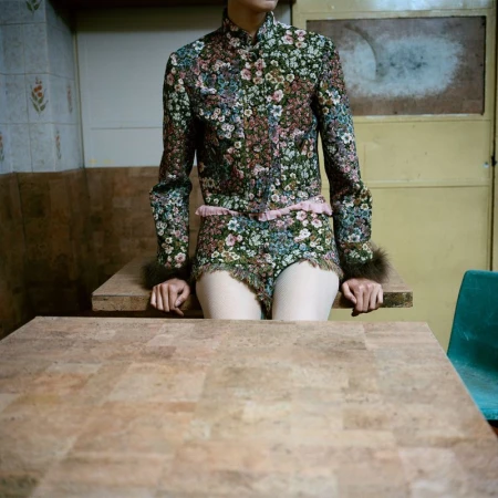 Model seated behind a table wearing a floral-patterned jacket and matching shorts with faux-fur cuff trim.