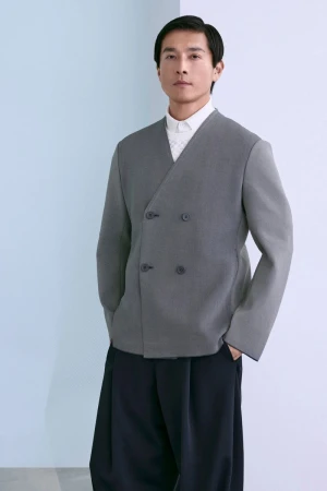 Model Daisuke Ueda in a grey double-breasted collarless knit jacket and dark wide-leg trousers against a pale studio backdrop.