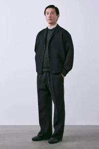 Model Daisuke Ueda in a black tailored jacket, textured knit sweater, and wide-leg trousers against a white studio background.