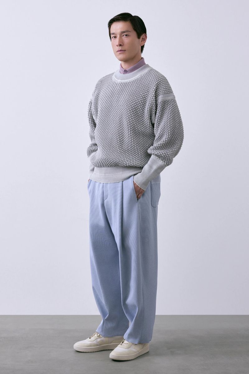 Model Daisuke Ueda standing in a textured grey knit sweater and wide-leg light blue trousers against a white studio background.