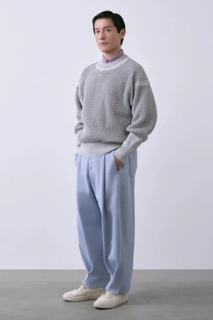 Model Daisuke Ueda standing in a textured grey knit sweater and wide-leg light blue trousers against a white studio background.