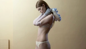 Model Lexie Tapper posing in cream lingerie and sheer grey opera gloves while holding a futuristic sneaker behind her neck.