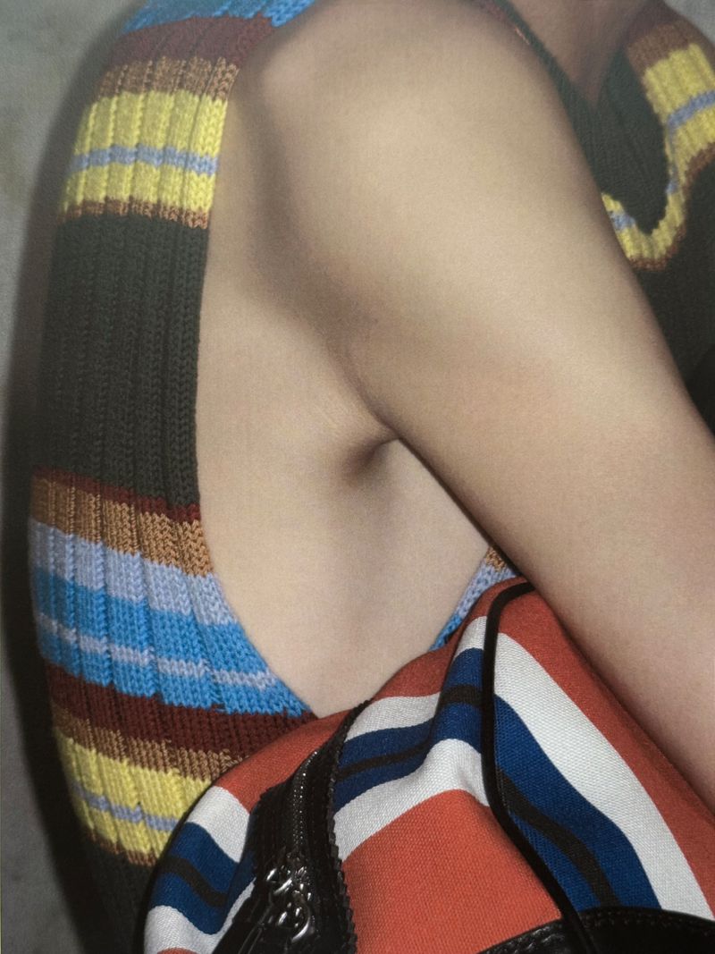Close-up of a fair-skinned person's torso wearing a striped knit top with a patterned purse or bag strap visible.