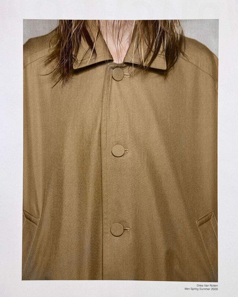 Close-up of a model wearing a camel brown button-up overcoat with a pointed collar and damp hair falling over the neckline.