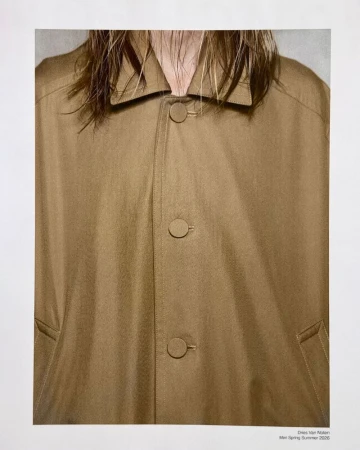 Close-up of a model wearing a camel brown button-up overcoat with a pointed collar and damp hair falling over the neckline.