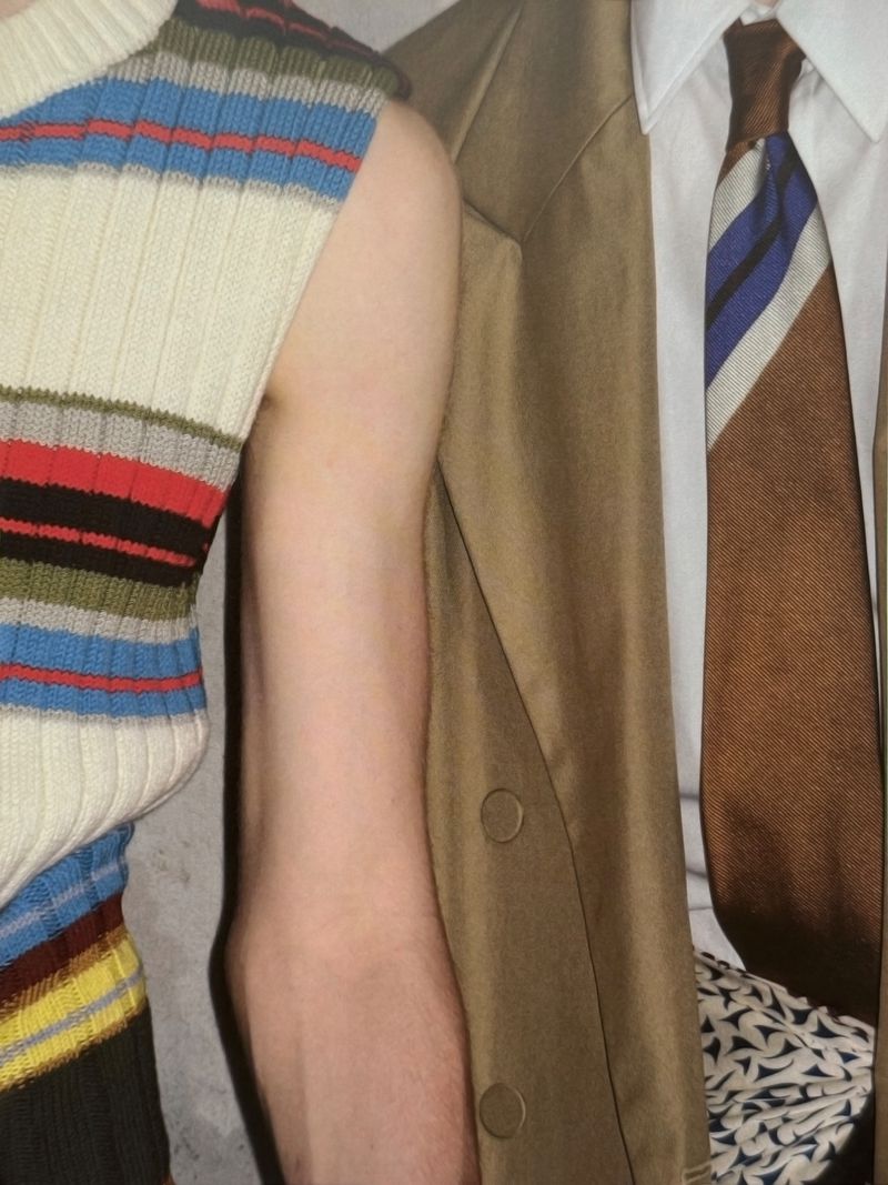 Cropped fashion shot featuring an arm with a knit top and a man in a suit and tie, focused on fabric textures and color composition.