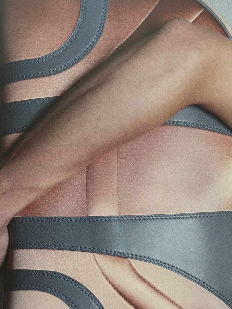 Torso of a person with an arm across the body, wearing an athletic-style garment with gray piping, in a close-up studio shot.
