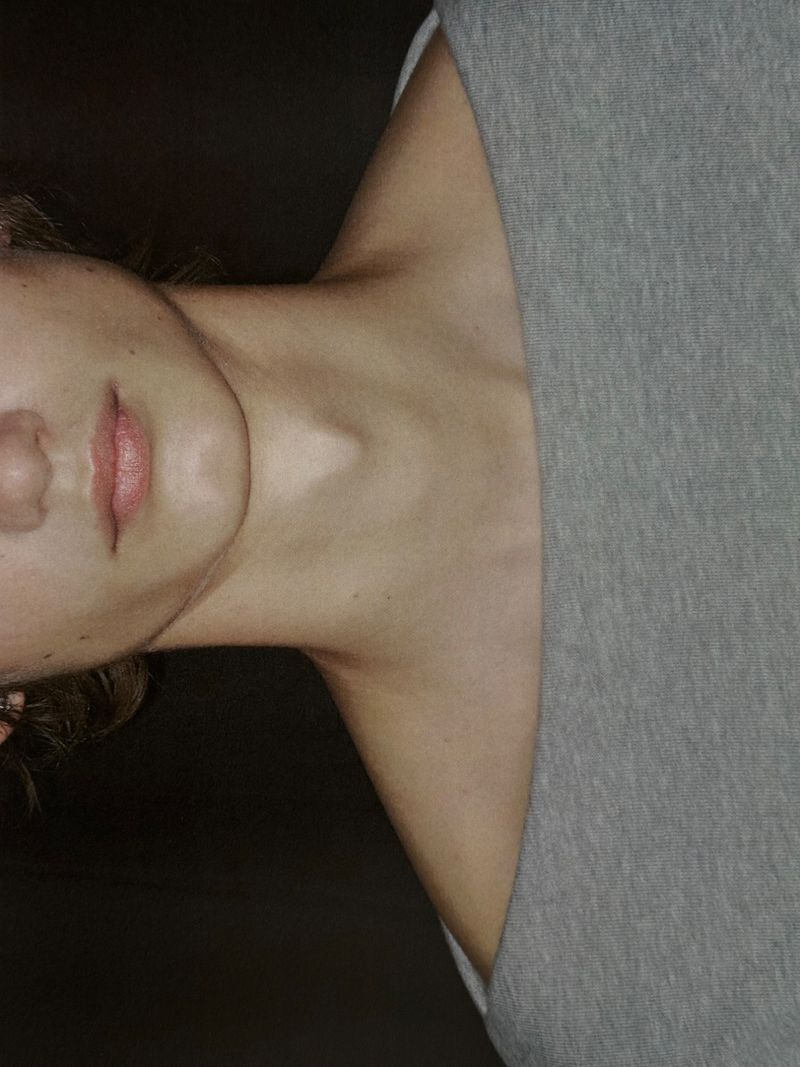 Close-up portrait of a fair-skinned person with pink lips and a gray shirt, highlighting the neck and shoulder area.