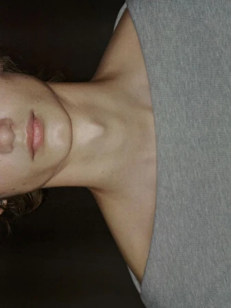 Close-up portrait of a fair-skinned person with pink lips and a gray shirt, highlighting the neck and shoulder area.