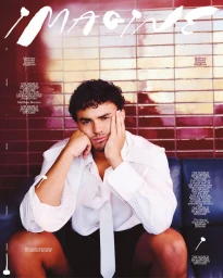 Actor Matthew Broome resting his face on his hand while seated on a blue sofa against a red tiled wall for IMAGINE Magazine.