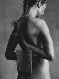 Model Heloise Guerin photographed from behind with braided hair, holding a metallic woven mini bag against a textured studio backdrop.