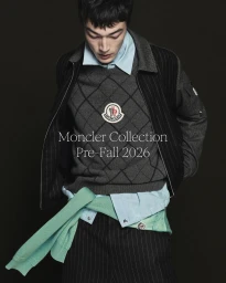 Pascal Thulin wearing a grey Moncler argyle knit sweater and pinstripe jacket against a black studio background.