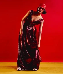 Model in dark sequin gown and red cap standing against a vibrant red backdrop for D Repubblica