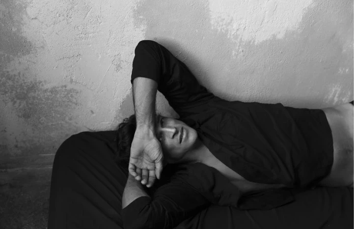 Black and white portrait of model Romulo Pires lying on a dark surface in an unbuttoned black shirt against a textured wall.