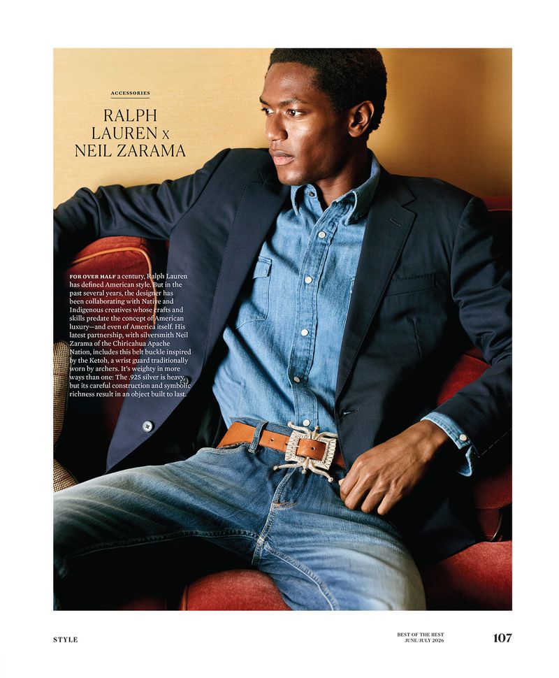 Hamid Onifadé seated on a red armchair wearing a navy blazer, denim shirt, blue jeans, and an ornate silver belt buckle.