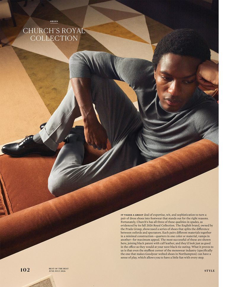 Model Hamid Onifade seated on a rust sofa wearing a grey knit top and trousers with black dress shoes for Robb Report U.S.