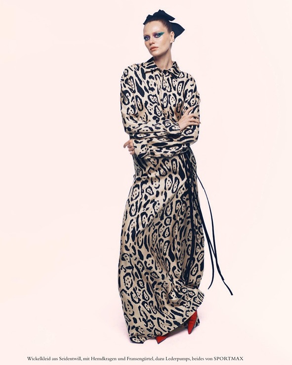 Model in long patterned dress and black hair bow against a pale background for Harper's Bazaar Germany