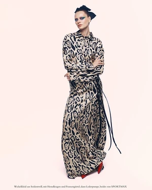 Model in long patterned dress and black hair bow against a pale background for Harper's Bazaar Germany