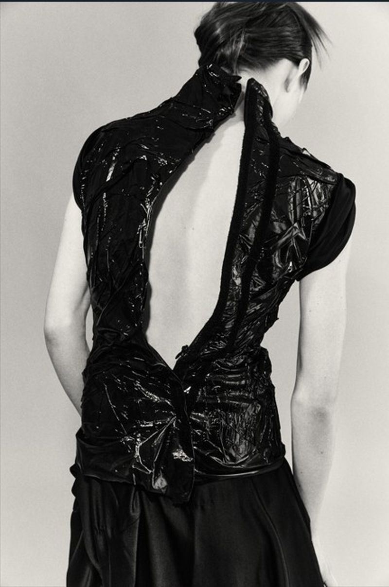 Model Wilda Rubin viewed from behind wearing a textured black high-neck open-back top in a monochrome studio setting.