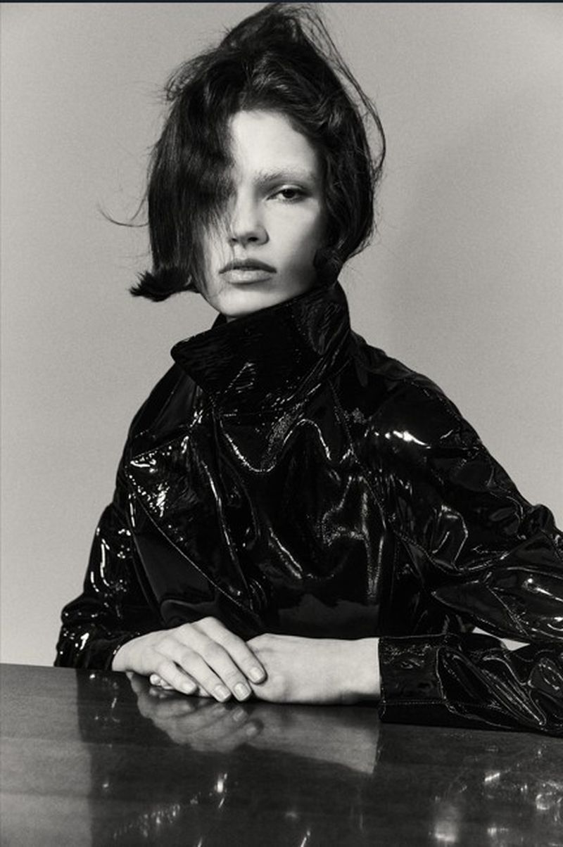 Model Wilda Rubin wearing a glossy black patent jacket with hands resting on a reflective surface in a monochrome portrait.