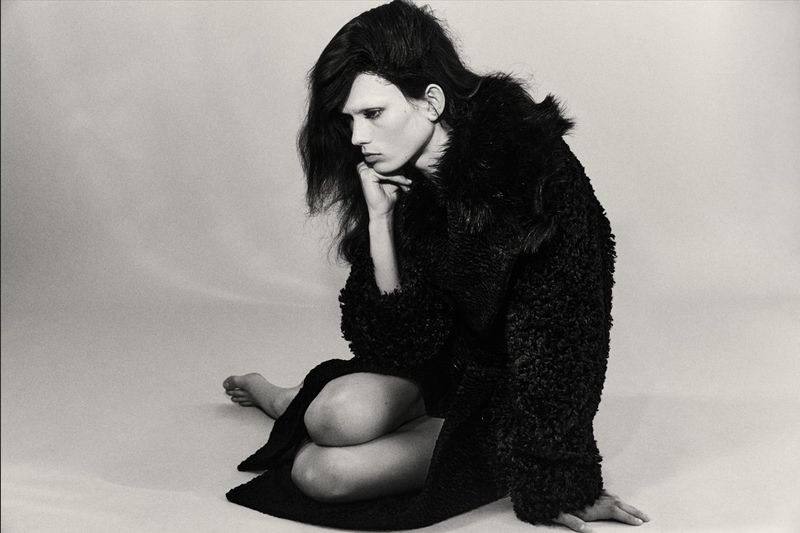 Model Wilda Rubin seated on a studio floor wearing an oversized black textured coat in a black and white editorial portrait.